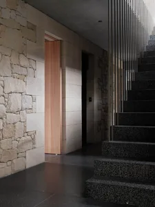 Modern interior design featuring concrete flooring, stone walls, and a wooden door with a metal stair railing.