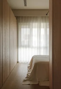 Minimalist bedroom featuring wooden shutters and glass panels, with soft lighting and neutral tones