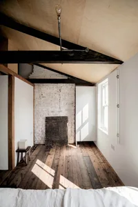 A minimalist bedroom with an angular ceiling, white brick wall, and wooden floor.