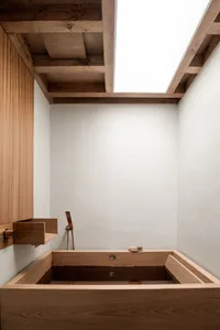A minimalist bathroom with a wooden bench, a skylight in the ceiling, and a faucet.