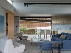 Modern living room featuring a concrete floor and walls, with a blue sofa and white accent chair.