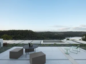 A modern rooftop terrace featuring glass railings, concrete floor, and a view of the blue sky.