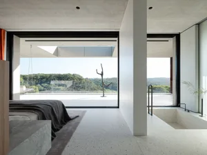 Modern bedroom featuring concrete flooring and walls, with a view of trees outside through large windows.