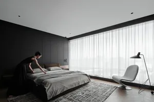 A modern minimalist bedroom featuring a bed with textured brown sheets and pillows, a gray armchair, and a floor lamp.