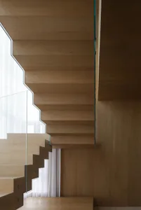 Modern wooden staircase with glass railings and white curtains in the background.