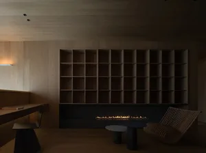 A modern minimalist living room with a large wooden bookshelf and a fireplace with a low flame.