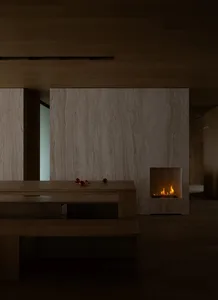 A modern living room with wood floors, taupe marble walls and a fireplace emitting a warm glow.