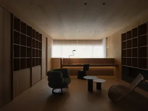 A modern minimalist living room with wooden furniture and flooring, featuring a green armchair, a black chair, and two coffee