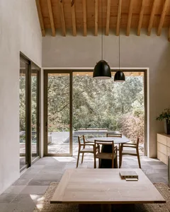 Modern minimalist dining room with wooden furniture and large windows connecting to the outdoors.