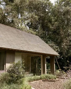 A modern hut with a shingled roof surrounded by lush greenery.