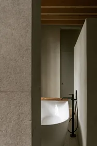 Modern minimalist bathroom featuring a freestanding white bathtub with a wooden shelf, industrial-style faucet, and concrete 