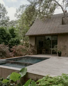 A modern backyard featuring a stone patio with a rectangular pool surrounded by lush greenery and wooden accents.