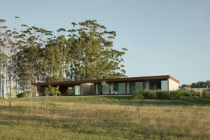 Modern residential house with large windows, wooden exterior, and glass walls surrounded by greenery.