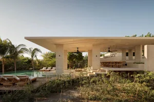 A modern residential structure with a concrete exterior and a large outdoor area featuring a pool and lounge chairs.
