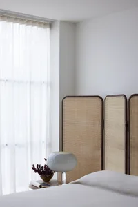 Minimalist bedroom featuring a white fabric screen behind a neatly made bed, with a clean and airy window curtain letting in 