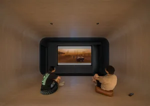 A minimalist home theater setup with two people sitting on floor cushions and watching a movie on a large screen.