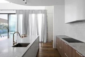 Modern kitchen featuring white countertops, grey cabinets, and large windows with sheer curtains.