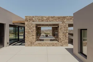 Modern minimalist patio with stone walls and concrete floor, featuring a dining table and chairs under an open-air roof, over