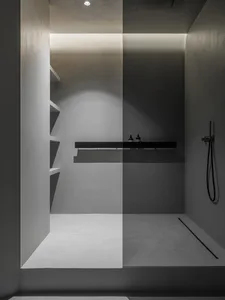 A minimalist shower area with concrete walls and floor, featuring a black and white color scheme and ambient lighting.