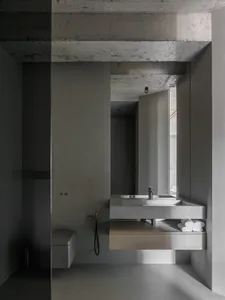 Modern minimalist bathroom with concrete walls and floor, featuring a floating sink with brushed metal fixtures and a towel s