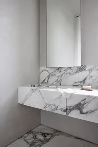 A minimalist bathroom with a marble sink and floor, featuring a sleek faucet and a white towel.
