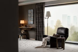 A modern living room featuring a leather couch, floor lamp, and large window with a cityscape view.