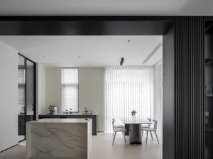 Modern minimalist kitchen featuring white marble countertops and a sleek dining area with vertical blinds.