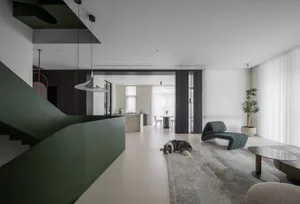 A modern minimalist living room with a grey couch and green rug, featuring a green staircase and a dog lying on the floor.