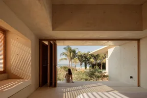 A modern residential bedroom with concrete walls and floor, featuring a view of the beach through an open window.