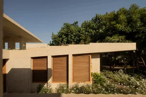A modern residential building with a concrete exterior, wooden shutters, and lush greenery.