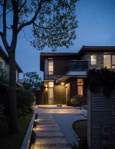 A modern residential home with wooden elements and brick walls at dusk, featuring a lit entranceway and a path leading to the