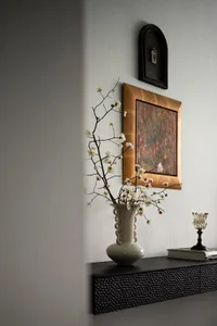 A modern shelf with a ceramic vase, metal vase, and framed art on a textured wall.