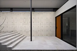 Modern residential entryway featuring a concrete and marble floor, with a wooden door and large windows.