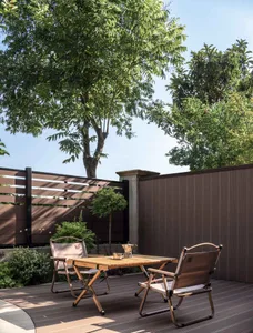 Outdoor teak dining table and chairs under a tree in a minimalist backyard.