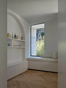 A minimalist living space featuring a window seat with a cushion and a curved wall shelf displaying colorful ceramic vases an
