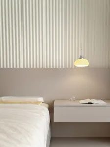 A modern minimalist bedroom featuring white bedding, a floating nightstand with a glass of water and an open book, and a pend