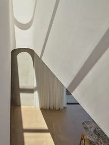 A modern, minimalist interior with textured concrete walls and a warm, natural light filter through sheer curtains.