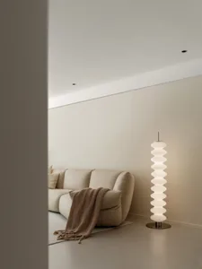 A minimalist living room with a beige sofa, neutral-toned floor lamp, and white walls.