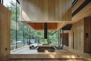 A modern wooden interior with an open-concept design, featuring a central fireplace and sliding glass doors overlooking a for