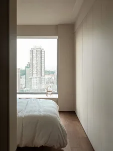 Modern minimalist bedroom with a wooden platform bed, overlooking a cityscape through a large window.