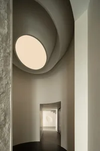 A minimalist interior with a concrete spiral staircase and a circular window letting in natural light.