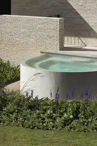 A minimalist landscape featuring a concrete planter with lavender plants and a brick wall in the background.