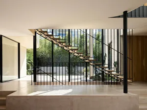 A modern interior space featuring wooden stairs with metal railings, concrete flooring, and a combination of natural and meta