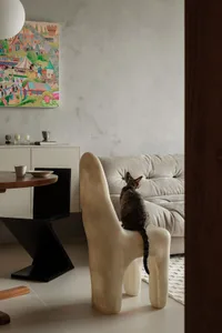 A modern minimalist living room featuring a concrete table, a white cushioned chair, and a framed cartoon painting hanging on