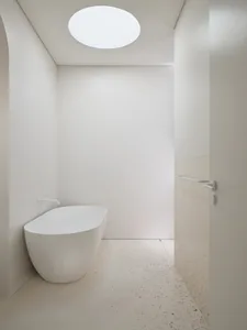 A minimalist bathroom with a white, oval-shaped bathtub, a terrazzo floor, and a circular skylight.