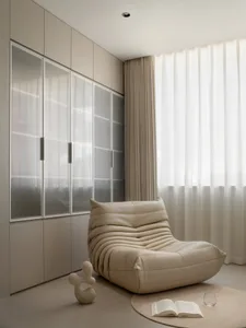 A modern living room with neutral-toned furniture, a large window, and a comfortable lounge chair.