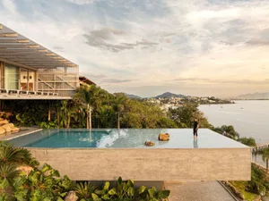 A modern residential exterior featuring a concrete structure with a rooftop pool overlooking the ocean and cityscape.