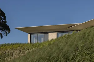 A modern residential exterior featuring stone cladding, large glass windows, and an extended roof overhang.