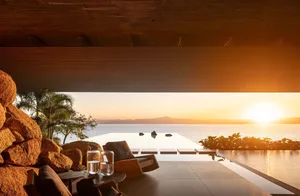 Modern residential exterior with wooden architectural elements and an infinity pool overlooking the sea at sunset.