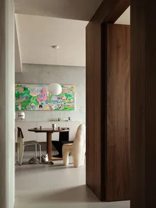 Modern dining room with a wooden table, concrete wall, and fabric chairs.